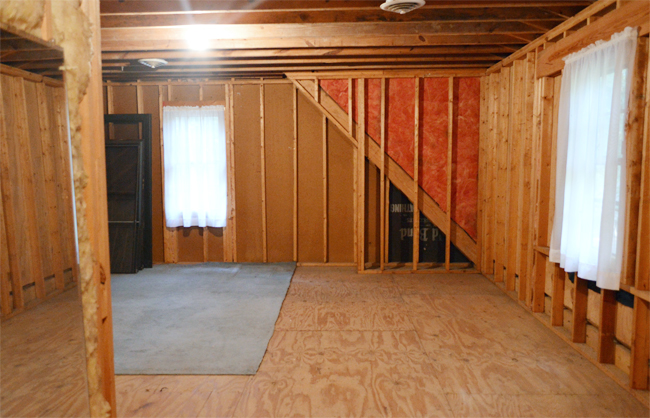 Unfinished attic storage room with exposed studs and curtained windows