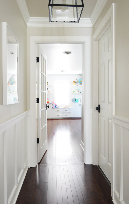 View into a bonus room playroom from hallway with white wainscoting and continuous wood flooring
