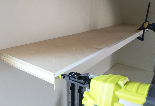 A Ryobi power nailer attaching face pieces of 1x2 pine wood board to thin white floating shelves in bonus room