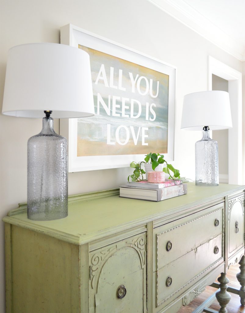 Dining room with vintage green buffet and green ivy plant under All You Need Is Love painting