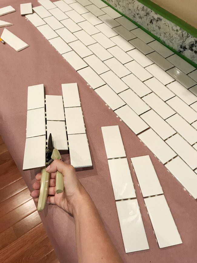 Sherry using scissors to cut tiles off subway tile sheet