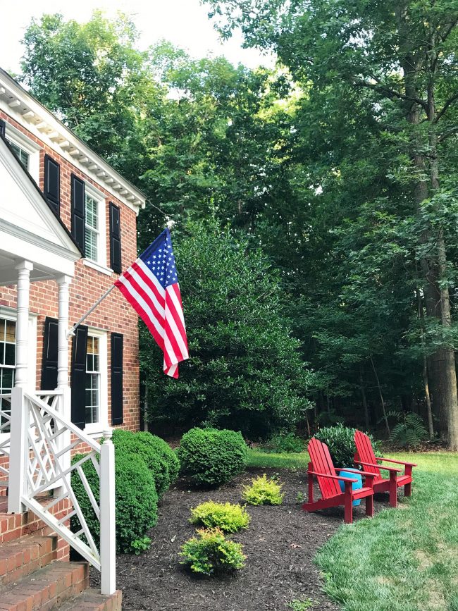 american flag on brick colonial home with red adirondak chairs