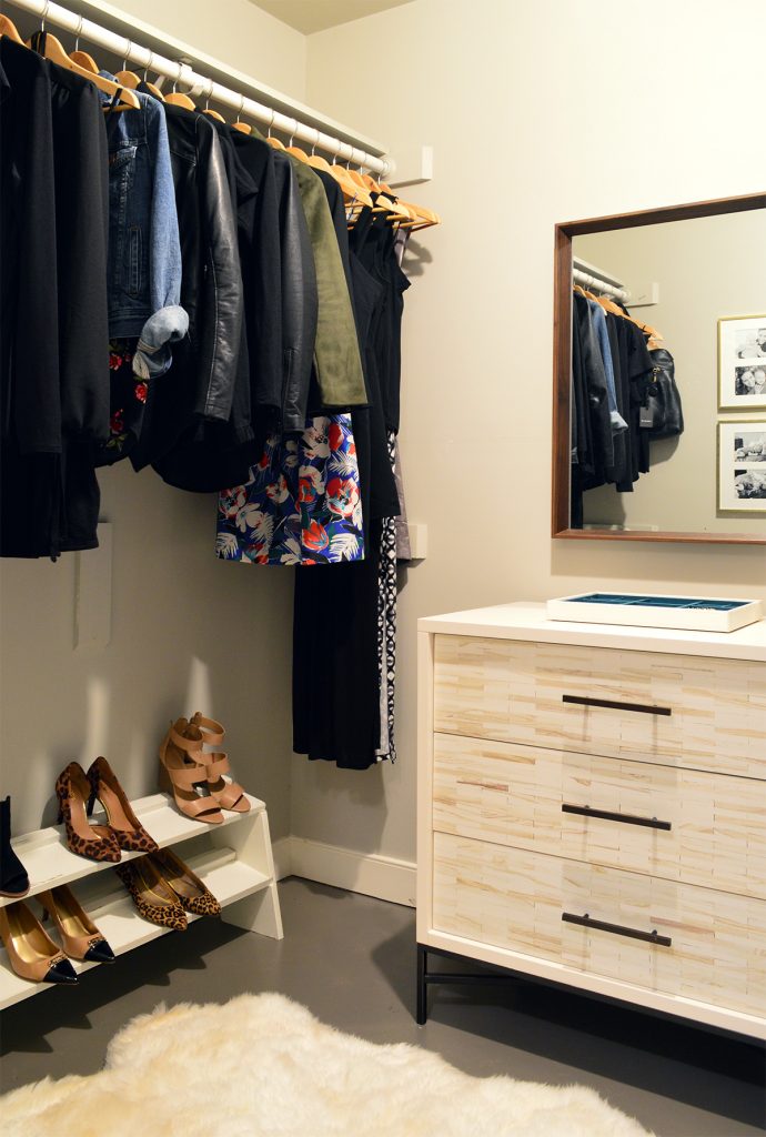 Walk in closet before renovation with dresser and hanging clothes bar