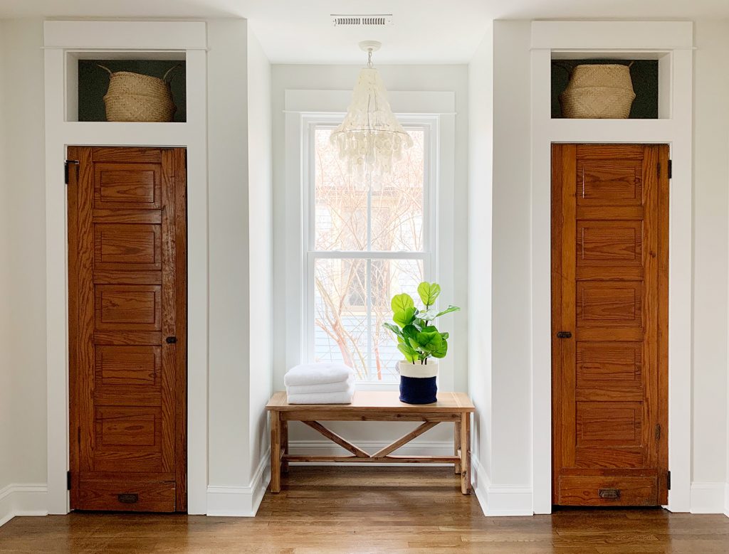 Faux fiddle leaf fig on bench between two closets under chandelier