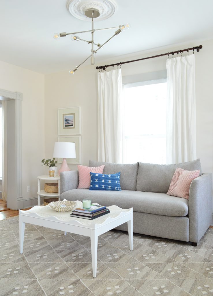 bright neutral living room gray sofa with white scalloped coffee table and modern chandelier