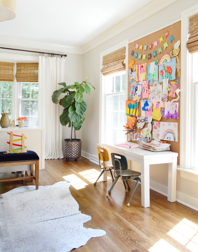 Office space with a kids desk with windows and a wall sized cork board above the kids desk 