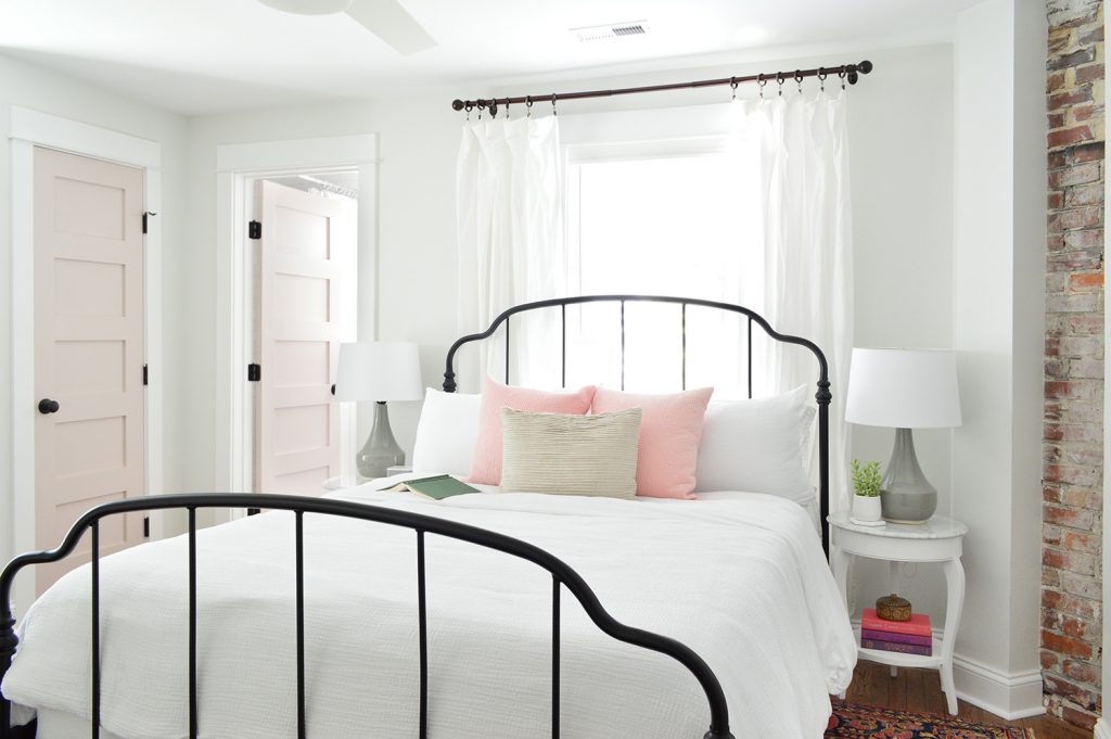 Historic Beachy Bedroom With Exposed Brick and Black Iron Bed And Pink Doors
