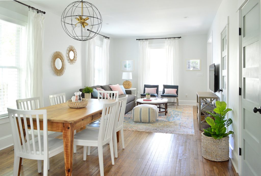 View Into Open Living And Dining Room With Wood Table And Cage Chandelier