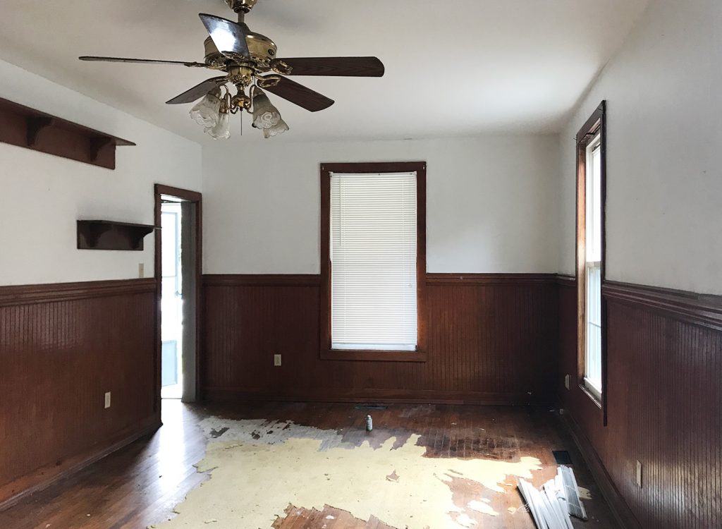 Before Photo Of Living Room With Dark Wood Paneling And Rug Adhesive Stuck To Floor