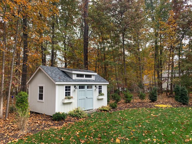 After View Of Charming White Shed With Blue Doors In Fall Foliage