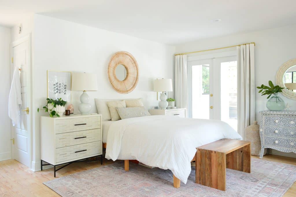 Florida bedroom with white walls and bedding with woven accents and traditional rug
