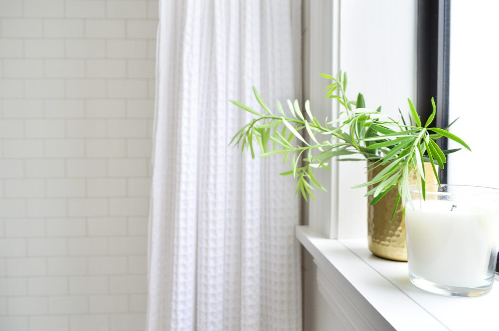 Bathroom sink with gold plant on window shelf by shower with subway tile