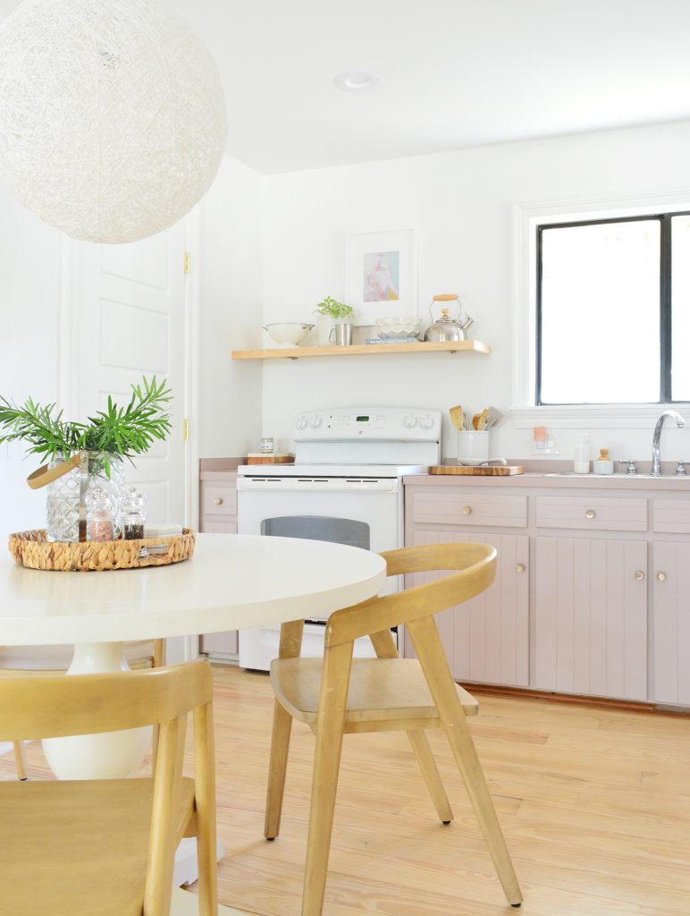 Simple white kitchen with mauve Artsy Pink cabinets and pedestal table