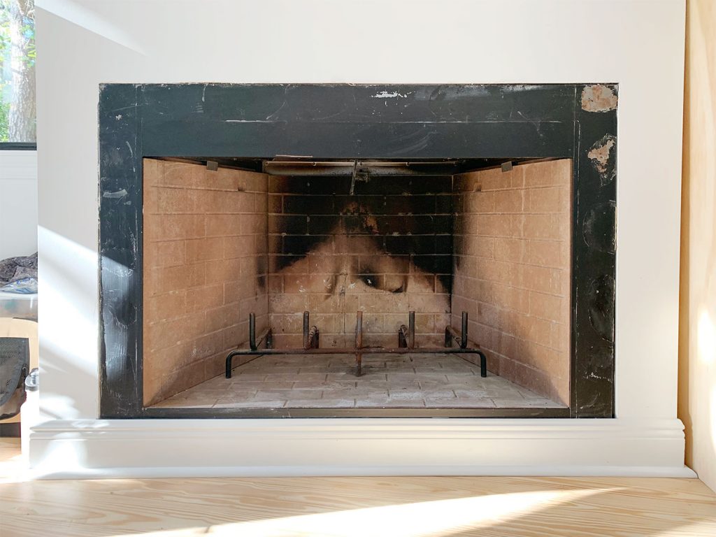 Before photo of fireplace with charred brick interior and patchy black metal surround