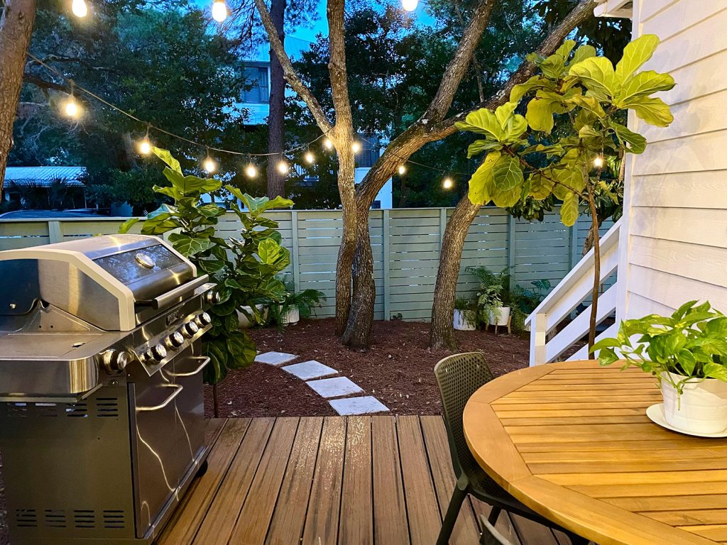 View looking out from kitchen porch with string lights glowing above grill and table for eating