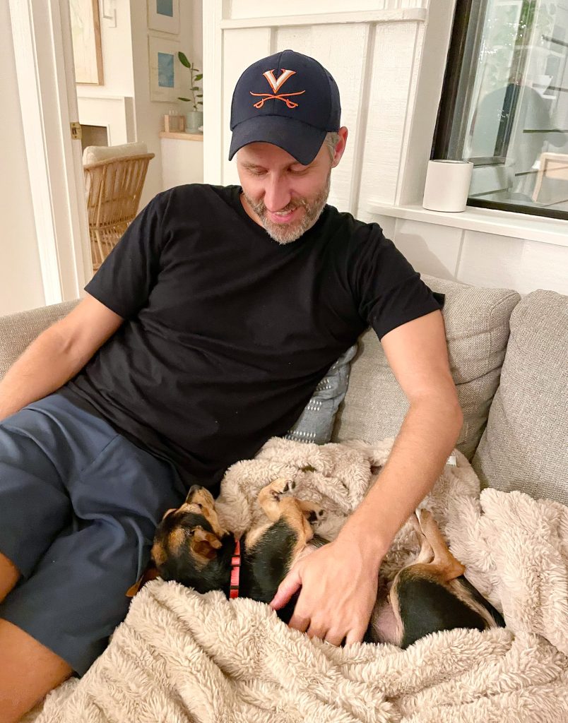 Chorkie mix snuggled in blanket next to John on loveseat