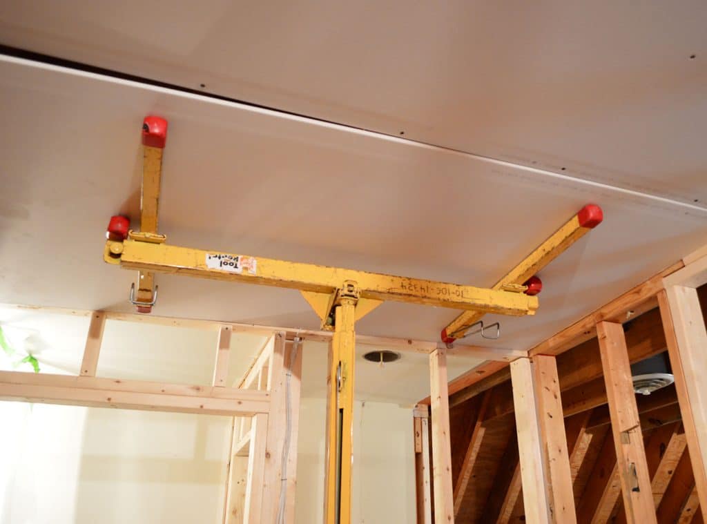 sheetrock panel held against ceiling of laundry room using drywall lift