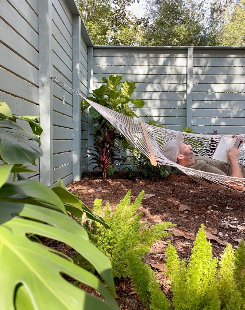 John deitado na rede do quintal lateral entre plantações tropicais