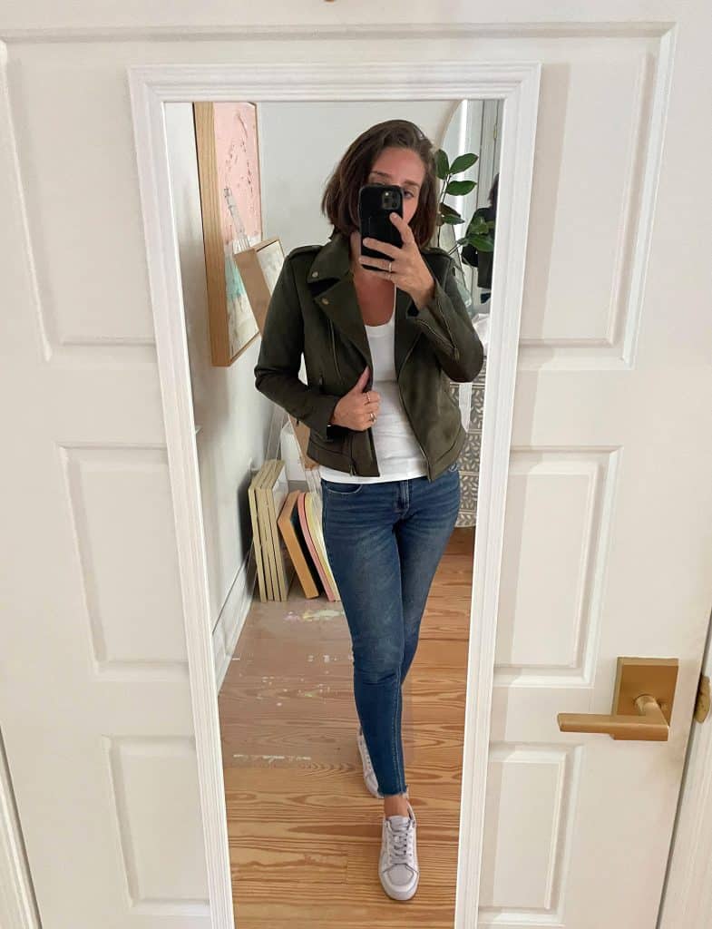 Sherry selfie in mirror at home with white tank top and green jacket with jeans and tennis shoes