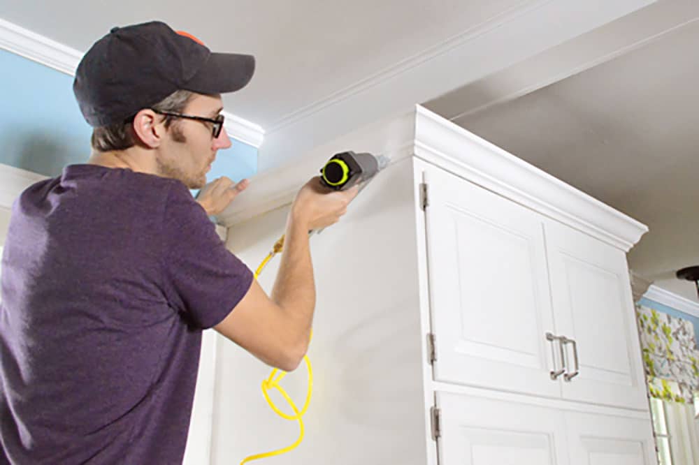 John using nail gun to attach crown molding to the top of the cabinets