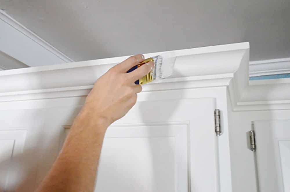 Painting crown molding on a kitchen cabinet with a short handled paint brush
