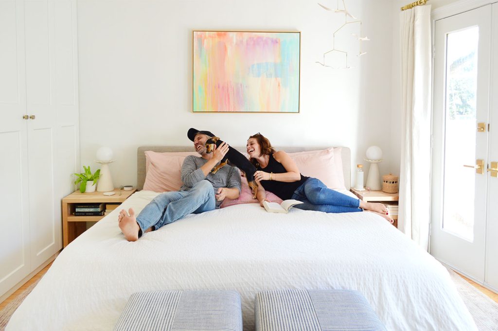 Dog Making John And Sherry Laugh On King Size Bed With White Bedding