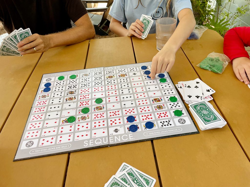 Family Playing Sequence Board Game On Outdoor Table