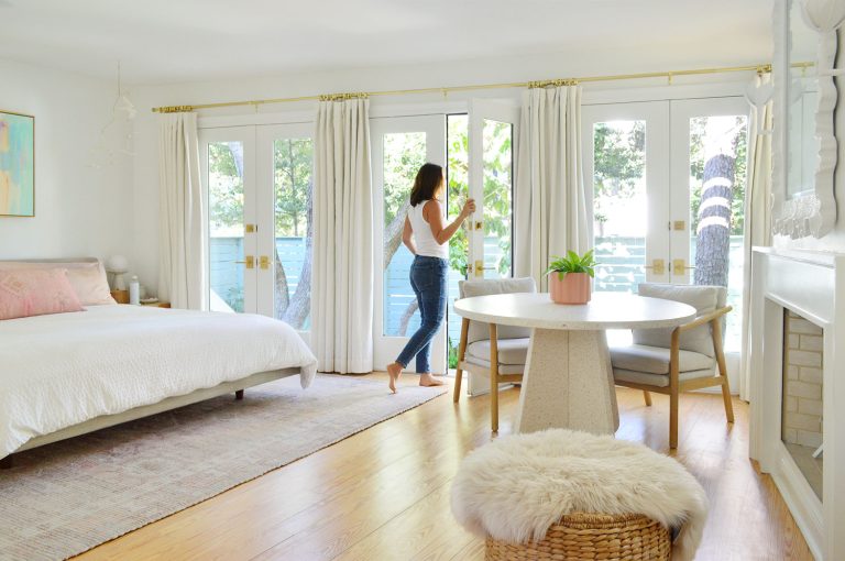 Woman Walking Through Wall Of French Doors In Bright Beachy Bedroom