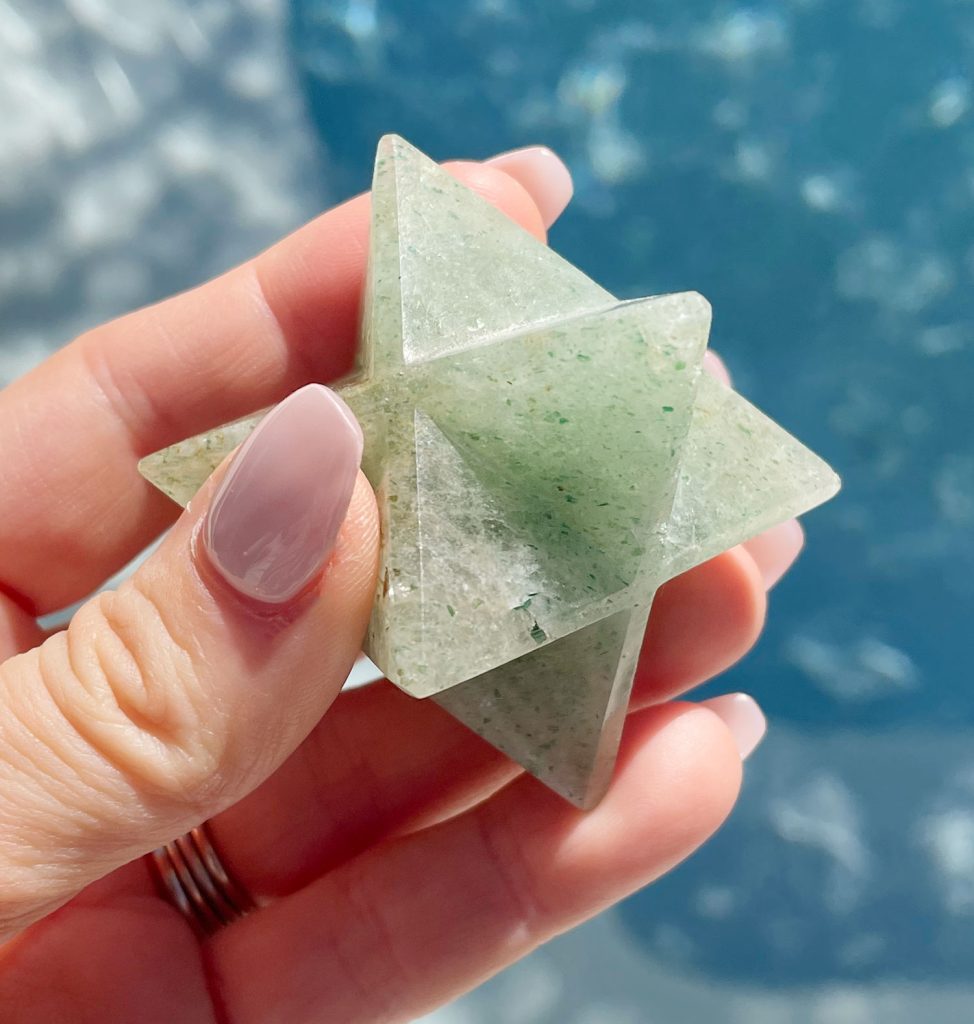 Hand holding green aventurine merkaba asteroid over water