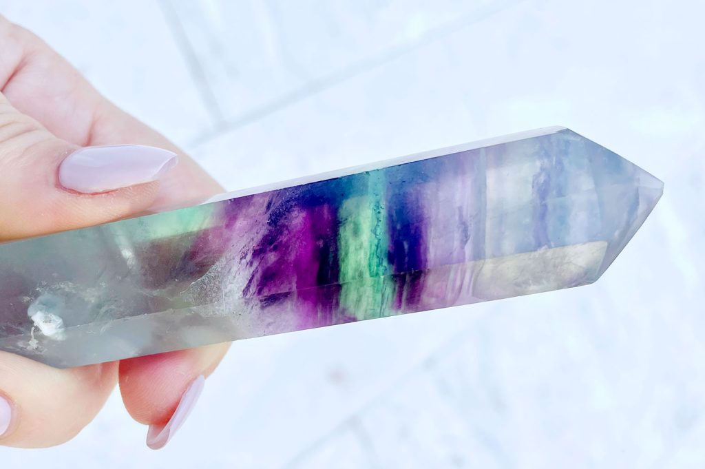 Hand holding crystal with purple green rainbow banding
