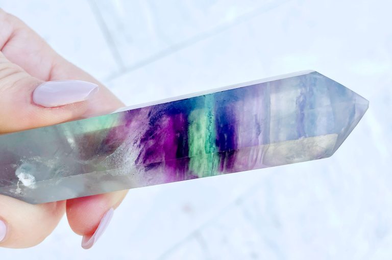 Hand holding crystal with purple green rainbow banding