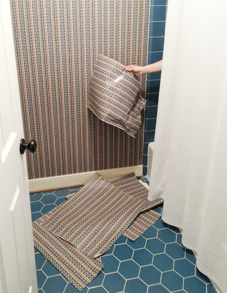 Hand removing wallpaper from shower in blue bathroom