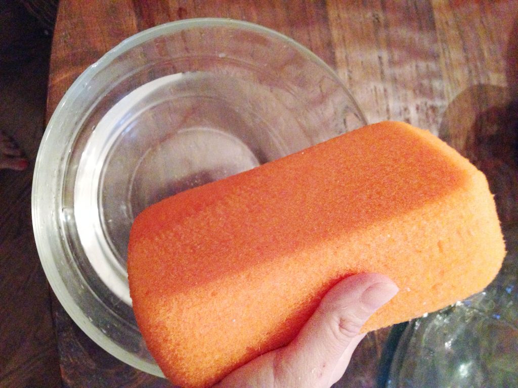 Hand holding orange sponge over bowl