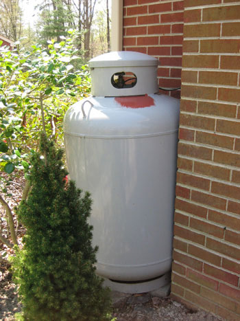 Metal utility propane tank behind painted red to match brick