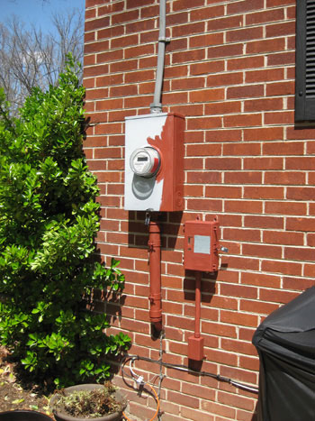 Half painted gray electrical utility meter box on back of brick ranch home