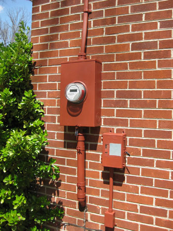 Electric meter utility box painted red to match brick red of home