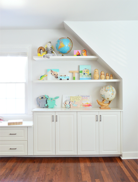 White floating shelves hung against angled wall and sloped ceiling in kids playroom bonus room