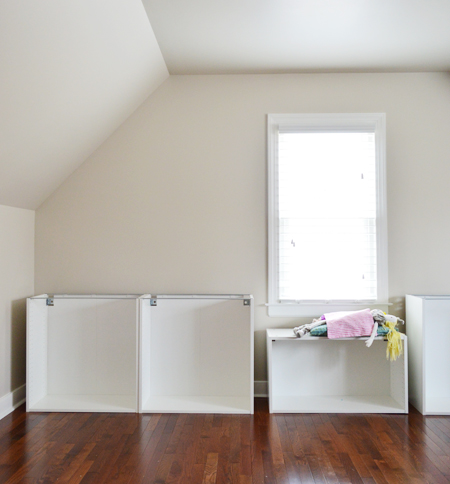 Room with sloped ceiling and Ikea cabinet boxes being built, with a girl's doll using one as a window seat