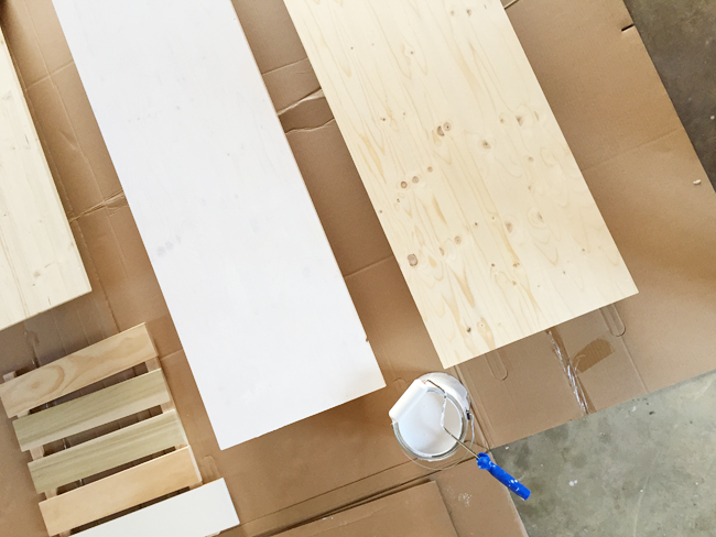 Wood project panels from Lowe's being primed and painted white using a small foam roller for use as countertops