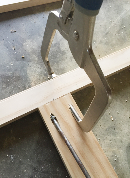 A Kreg jig clamp being used to secure two pieces of wood together at a right angle using a pocket hole screw