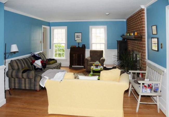 living room before staging with blue walls brick fireplace and lot of furniture