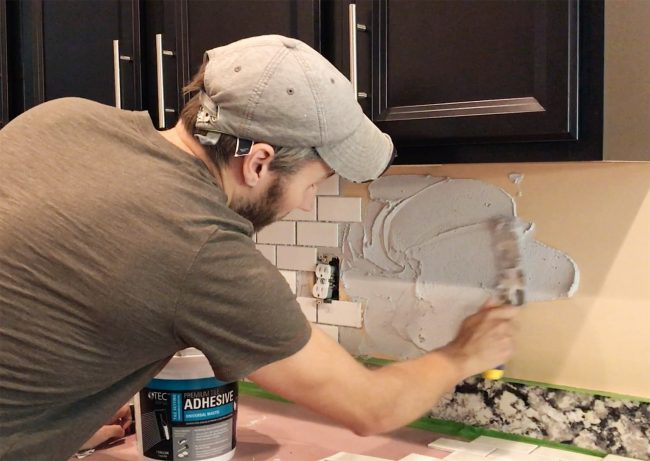 John spreading mastic adhesive on backsplash wall in kitchen