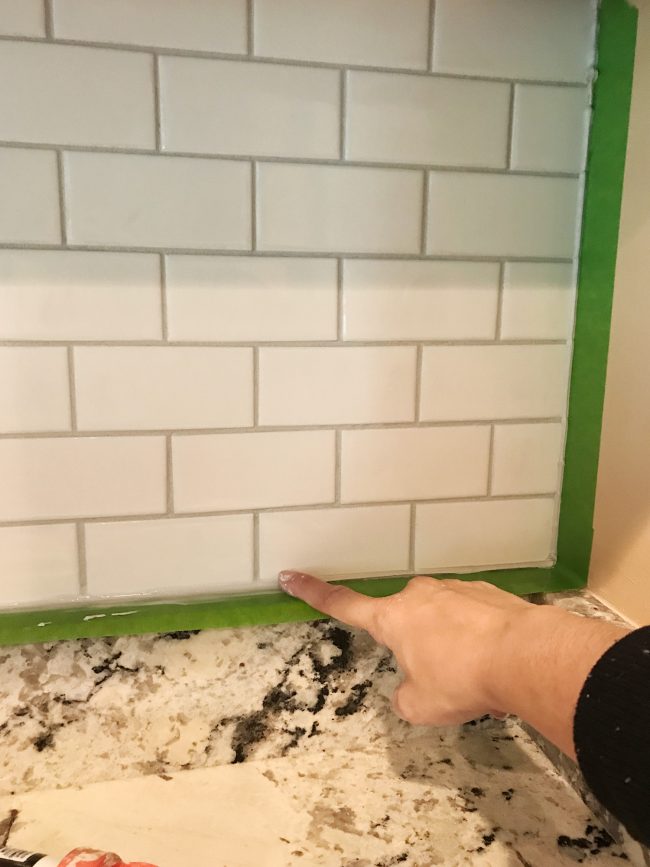 Sherry spreading caulk with finger along edges of installed backsplash