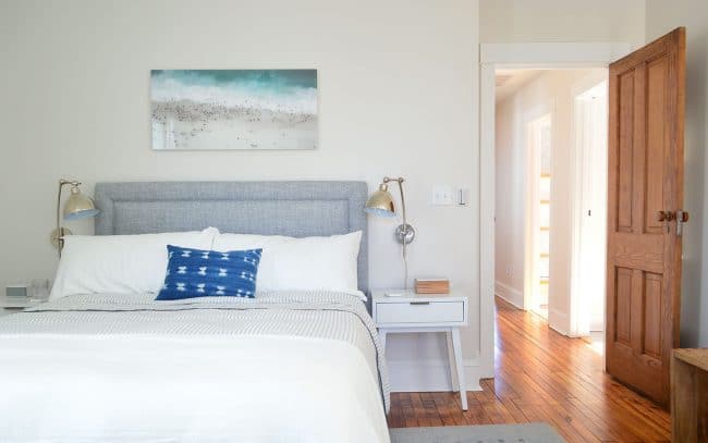 After Photo Of Beach House Back Bedroom With Gray Tufted Headboard And Beachy Artwork