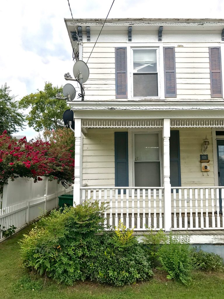 Half View Of Duplex Before Renovation With Satellite Dishes On Porch