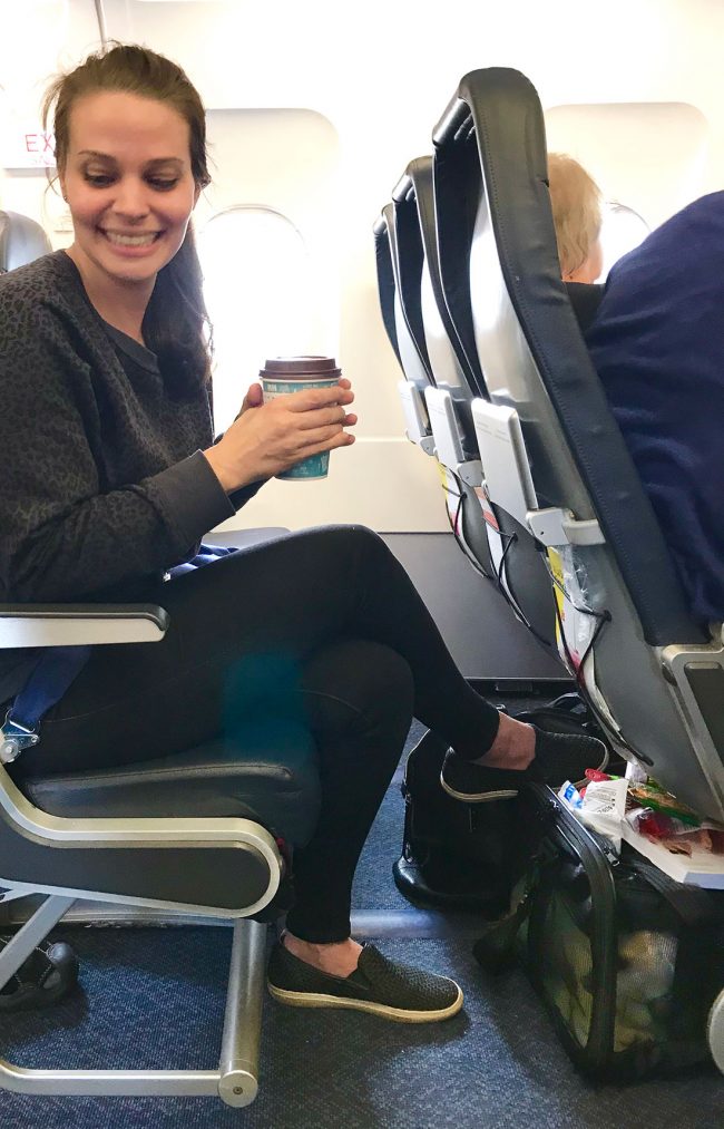 Sherry sitting on plane with dog carrier under seat in front of her