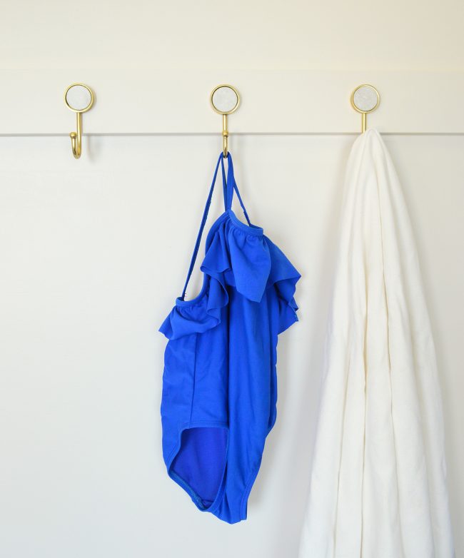 three gold hooks on diy rail with towel and bathing suit