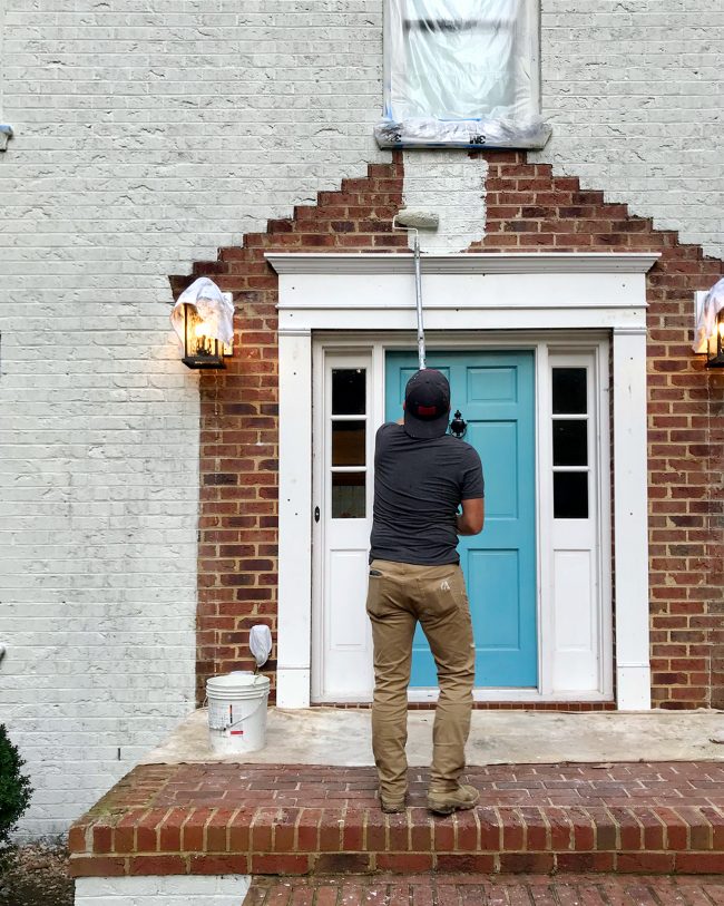 painter painting the front porch of a brick house white