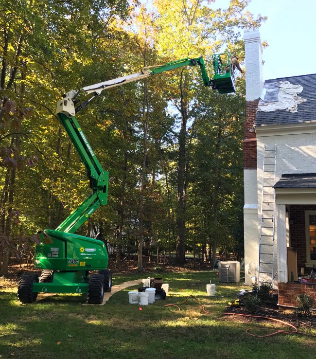 large lift crane raised to paint chimney of brick house