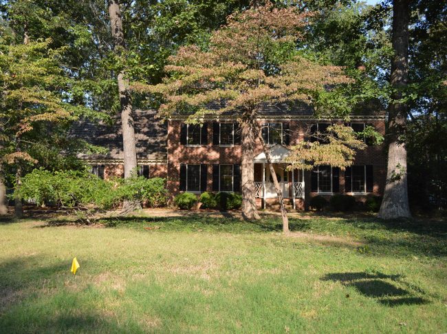 before photo of brick house covered by trees 